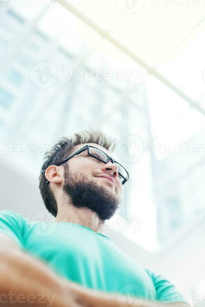 un hombre con lentes y un barba en pie en frente de un edificio foto