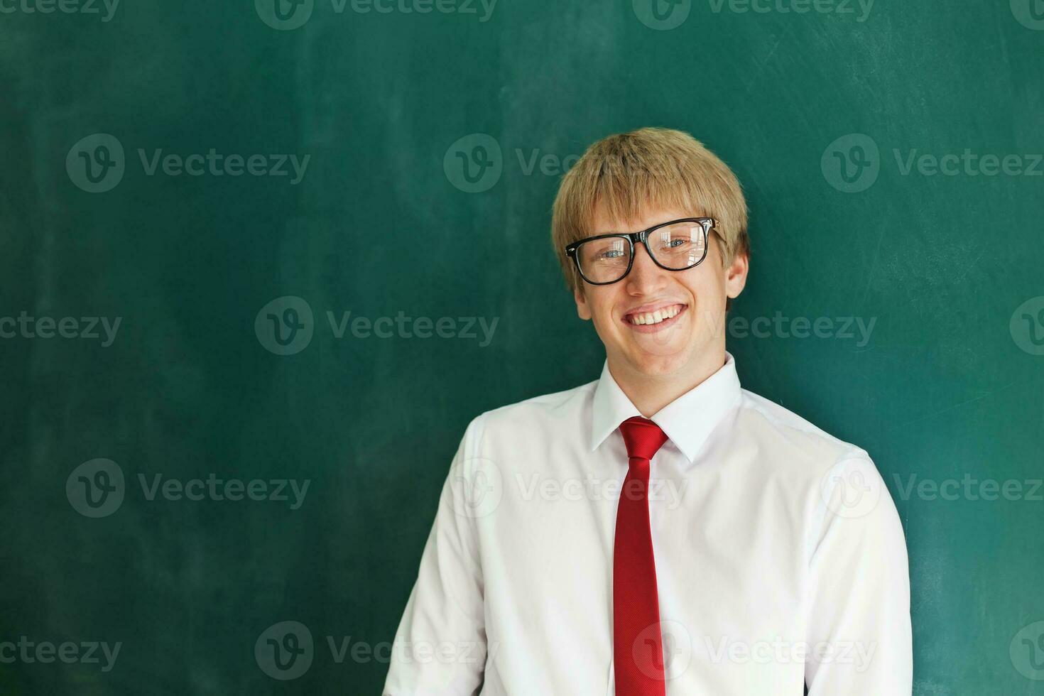 a young man in glasses and a tie standing in front of a blackboard photo