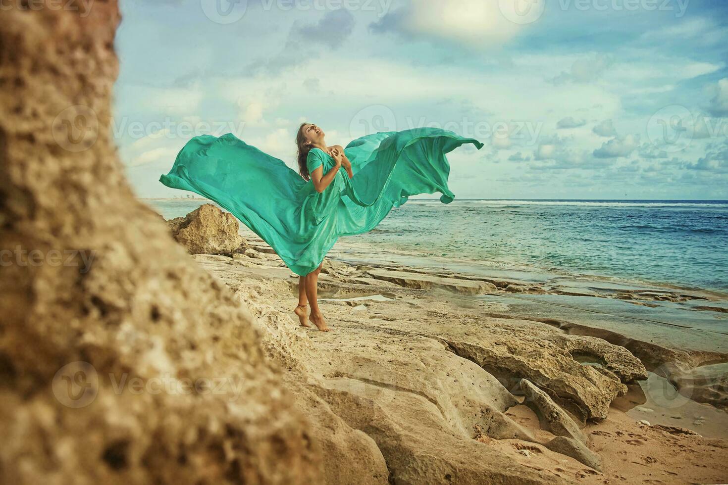 a woman in a green dress standing on a rocky beach photo