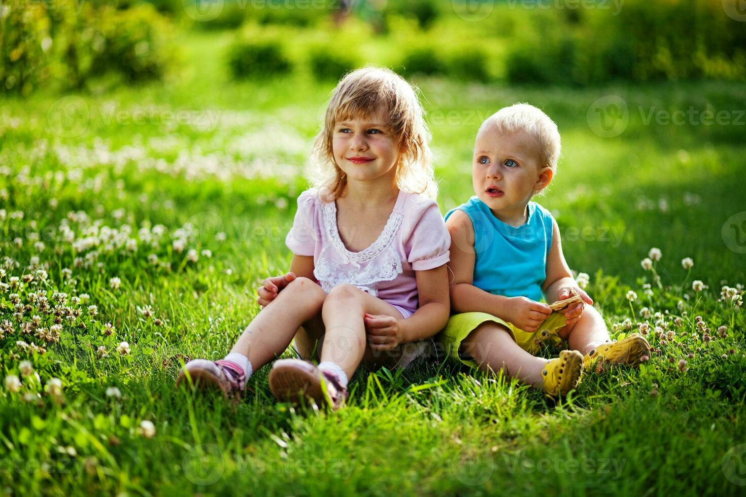 two children sitting on the grass in a field photo