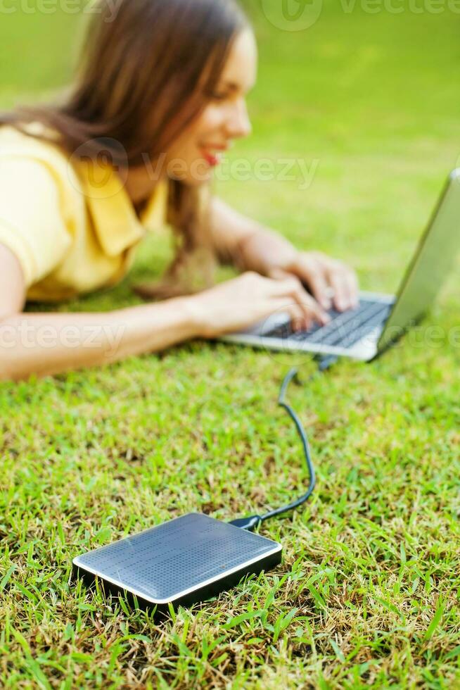 woman using hard drive disk to backup her data while lying down relaxed on a grass photo