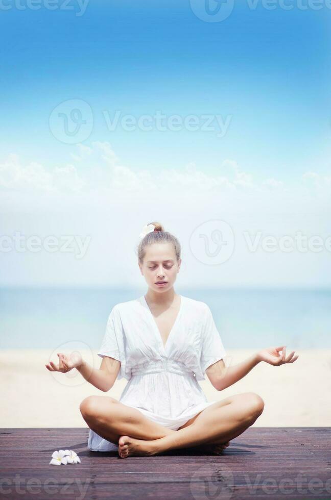 a woman meditating on the beach in a white dress photo