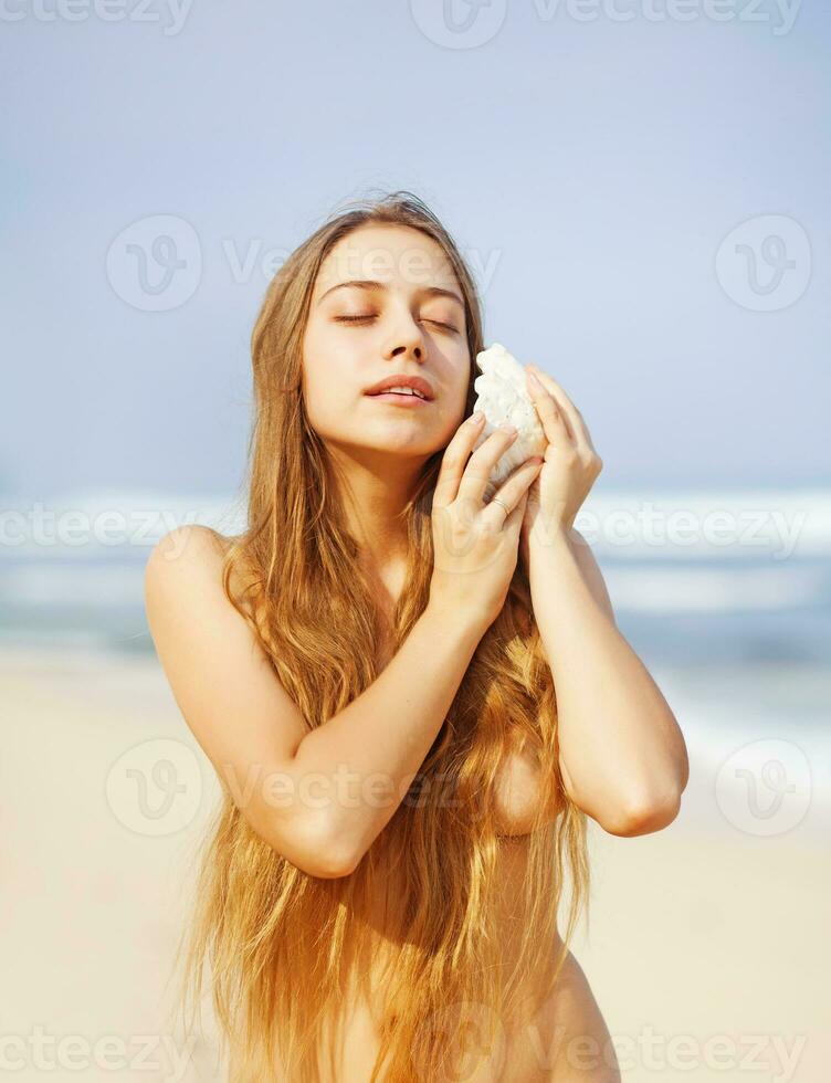 a naked woman holding a shell on the beach photo