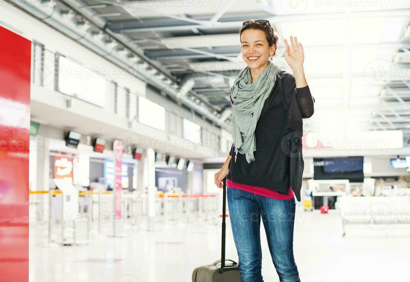 a woman with a suitcase waving at the camera photo