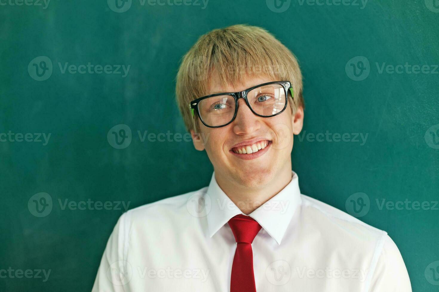 a young man wearing glasses and a tie standing in front of a blackboard photo