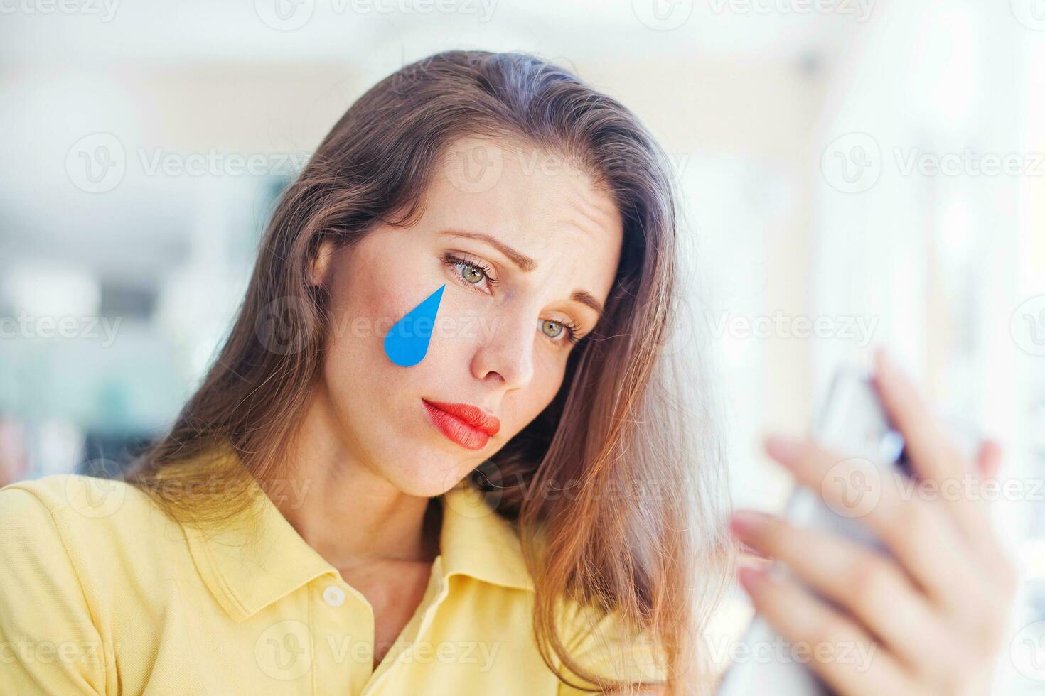 a woman with a tear on her face is looking at her phone photo