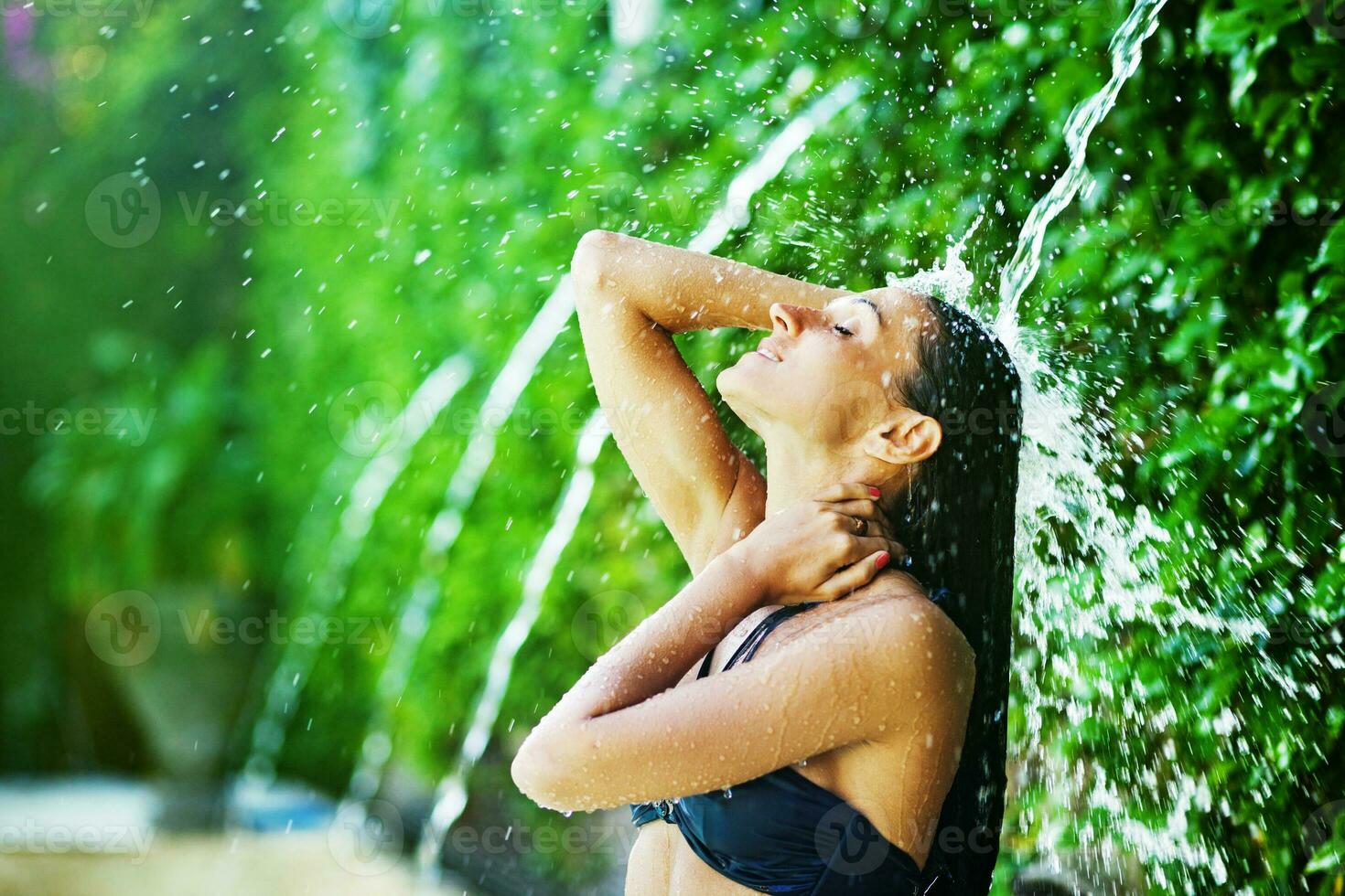 a woman in a bikini is standing under a waterfall photo