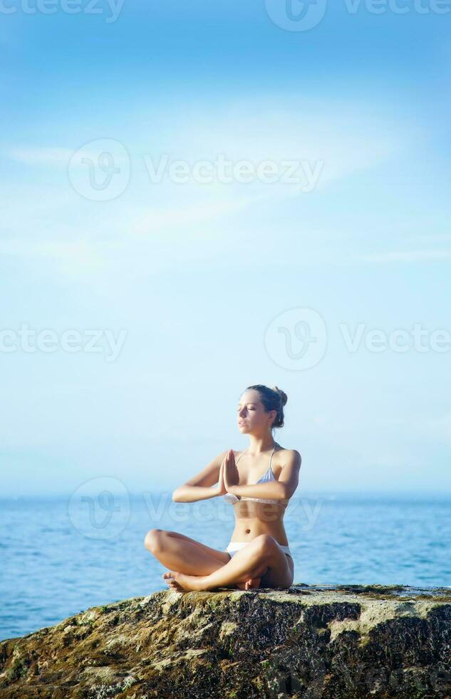 a woman in a yoga pose on a rock by the ocean photo