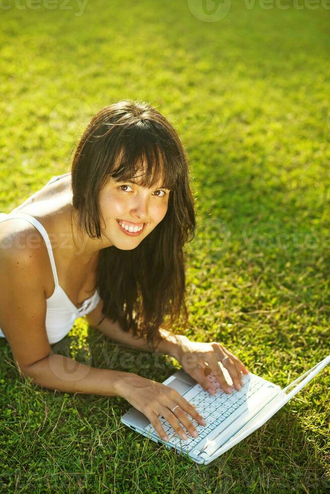 a woman laying on the grass with a laptop photo