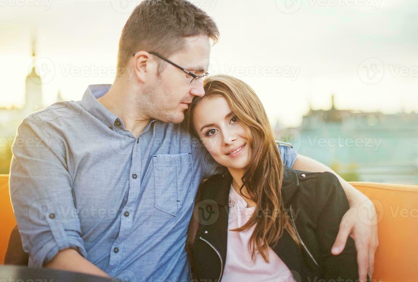 a man and woman sitting on a bench in front of a city photo