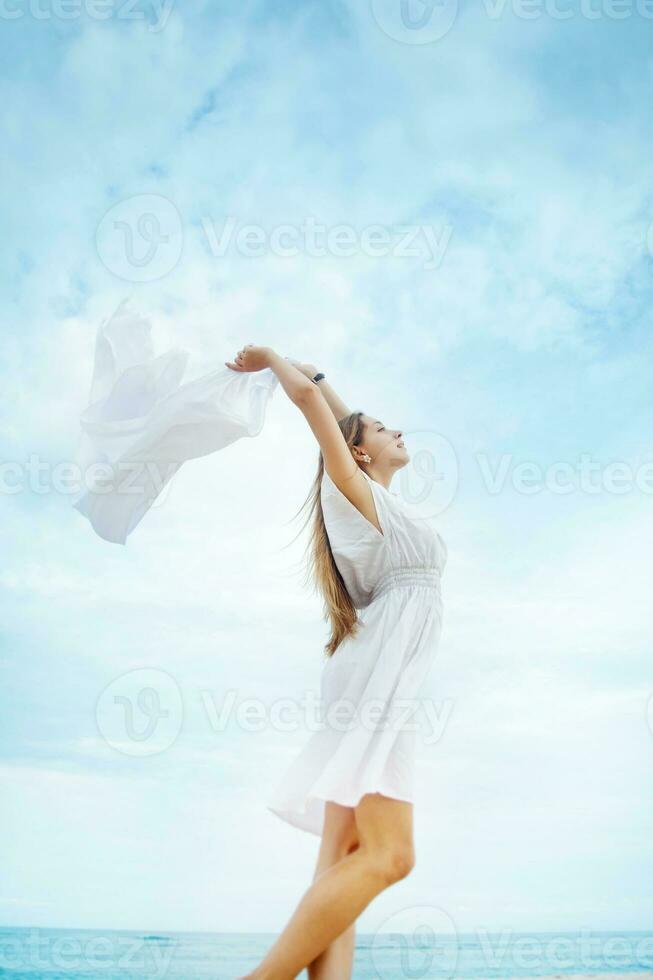 a woman in a white dress standing on the beach with a white cloth photo