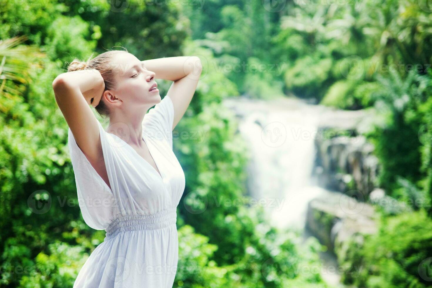 a woman in a white dress standing in front of a waterfall photo