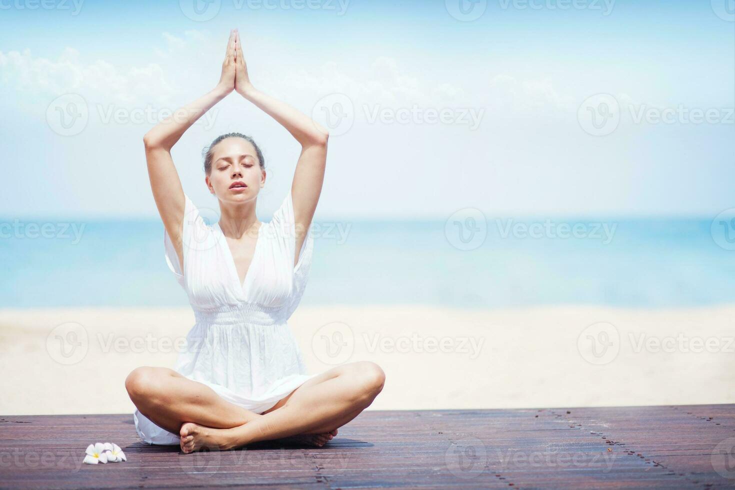 a woman in a white dress is doing yoga on the beach photo