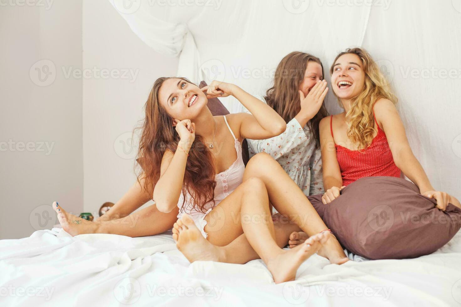 three women sitting on a bed laughing and talking photo