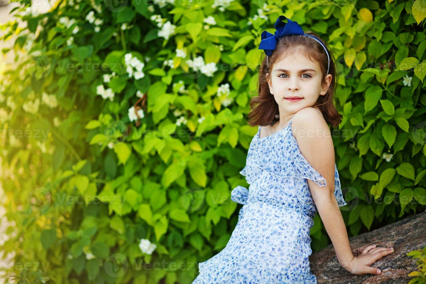 a little girl in a blue dress sitting on a rock photo