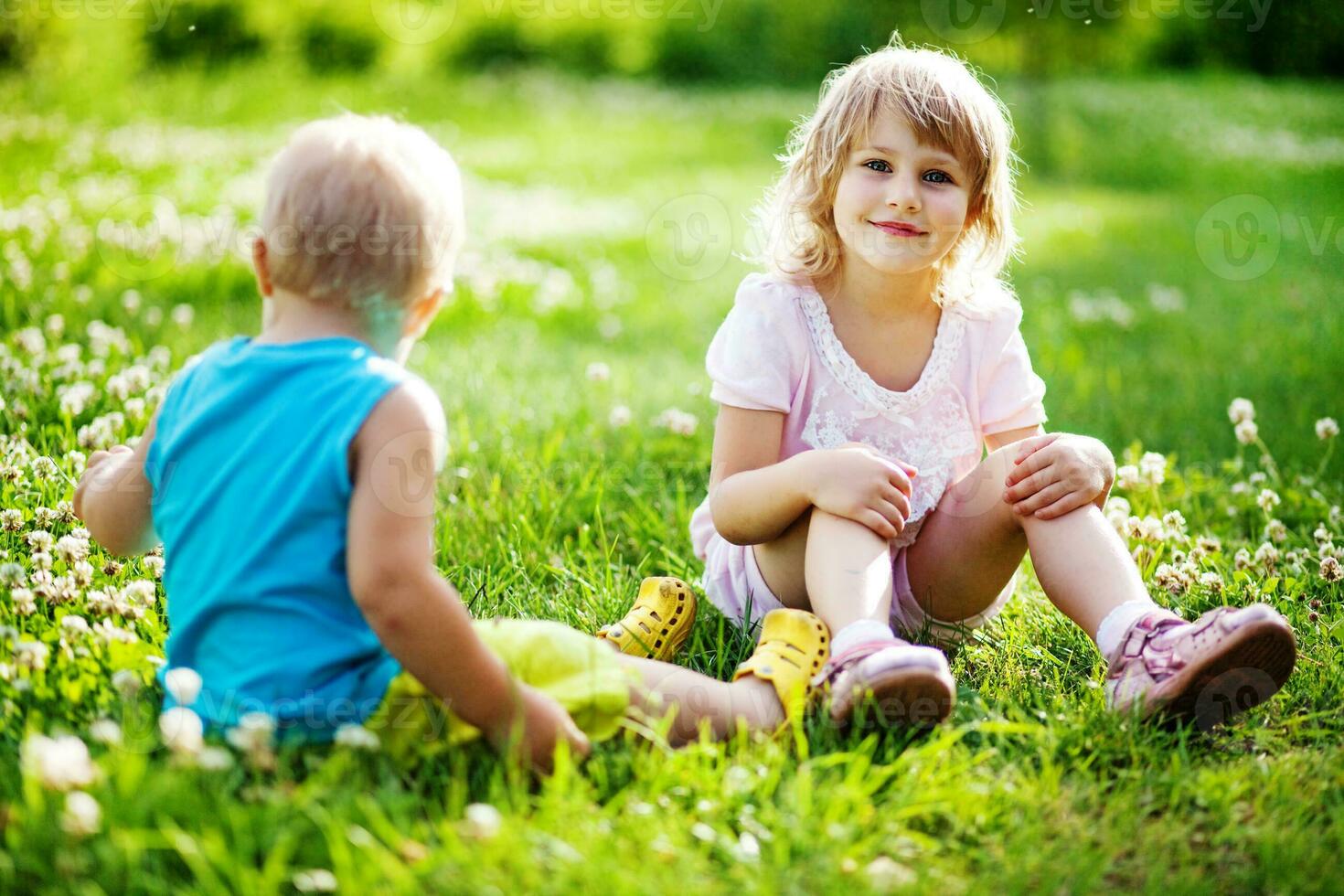 two children sitting on the grass in a field photo