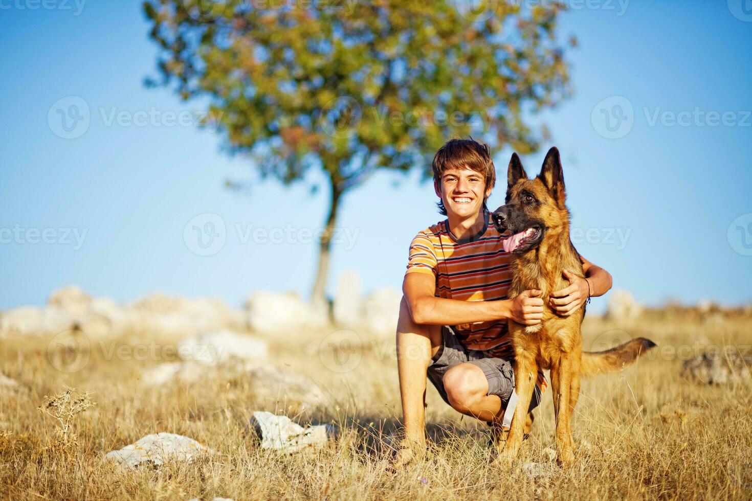 a young man kneeling with his dog in a field photo