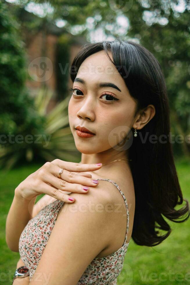 an Asian woman in a patterned dress posing with her hands in a garden photo