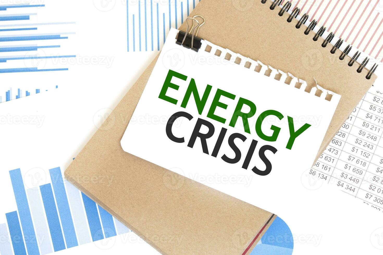 Text ENERGY CRISIS on white paper sheet and brown paper notepad on the table with diagram. Business concept photo