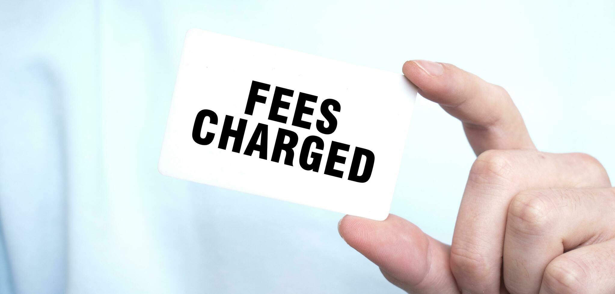 Man in blue sweatshirt holding a card with text FEES CHARGED, business concept photo