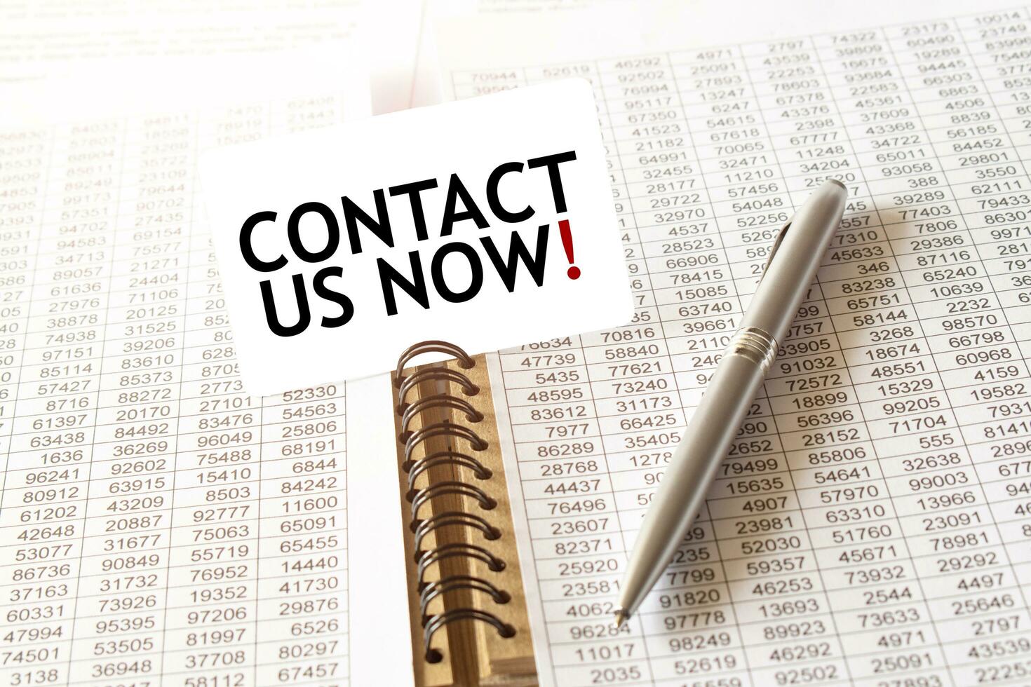 Text CONTACT US NOW on paper card, pen, financial documentation on table photo