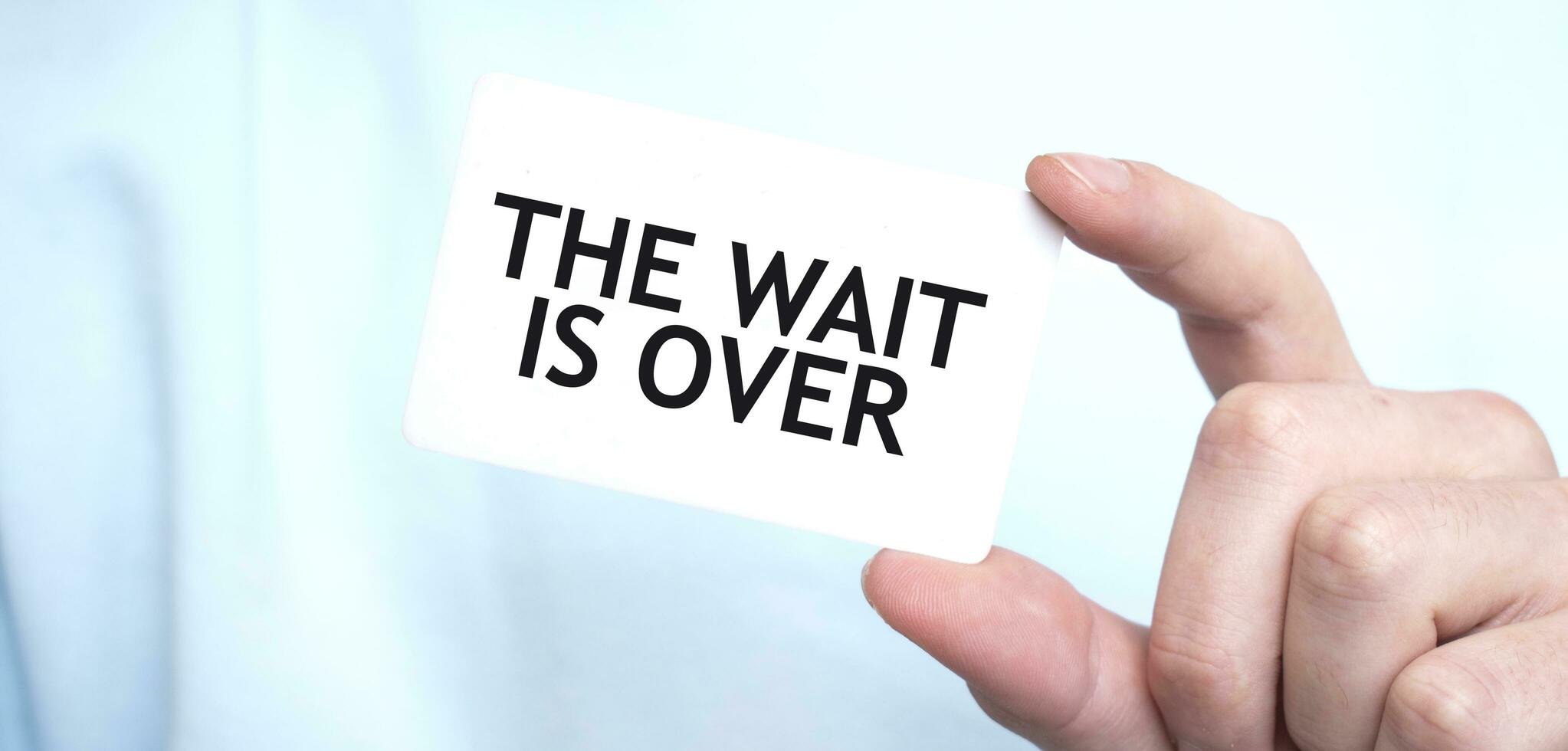 Man in blue sweatshirt holding a card with text THE WAIT IS OVER, business concept photo