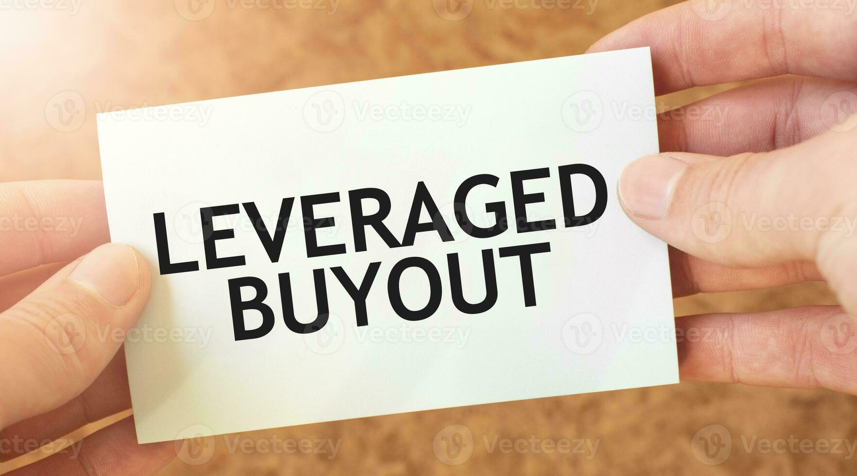 LEVERAGED BUYOUT word inscription on white card paper sheet in hands of a businessman. recap concept. red and white paper photo