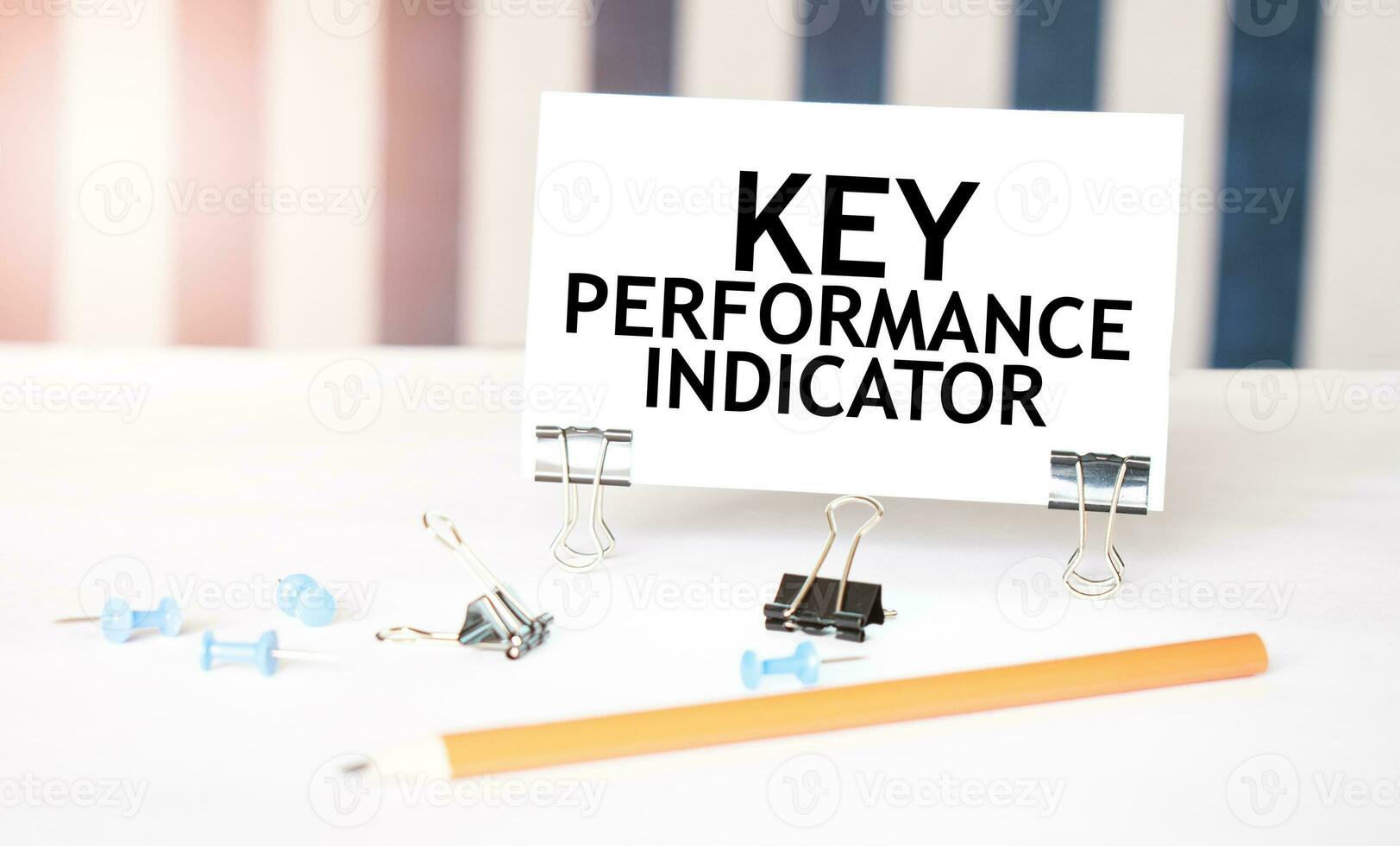 KEY PERFORMANCE INDICATOR sign on paper on white desk with office tools. Blue and white background photo