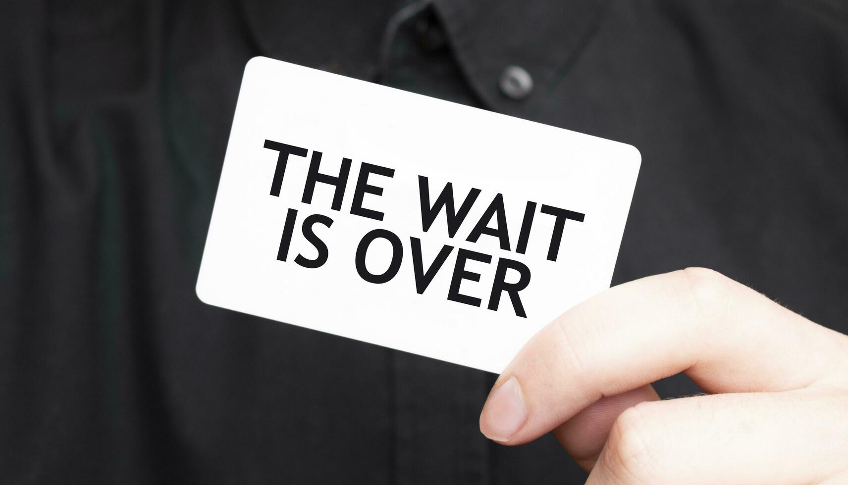 Businessman holding a card with text THE WAIT IS OVER, business concept photo