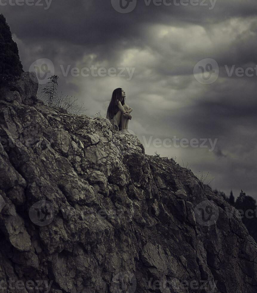 a woman sitting on top of a mountain with dark clouds photo