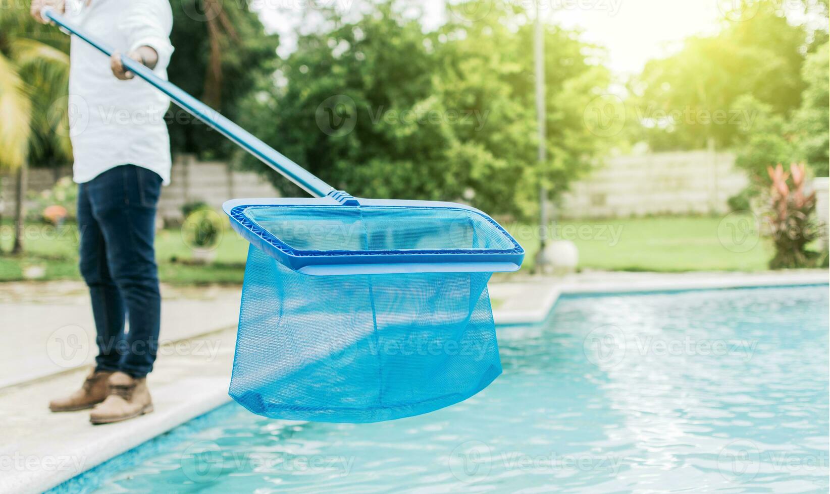 hombre limpieza el piscina con el desnatadora, un hombre limpieza piscina con hoja desnatadora. persona con desnatadora limpieza piscina, manos participación un desnatadora con azul piscina en el antecedentes foto