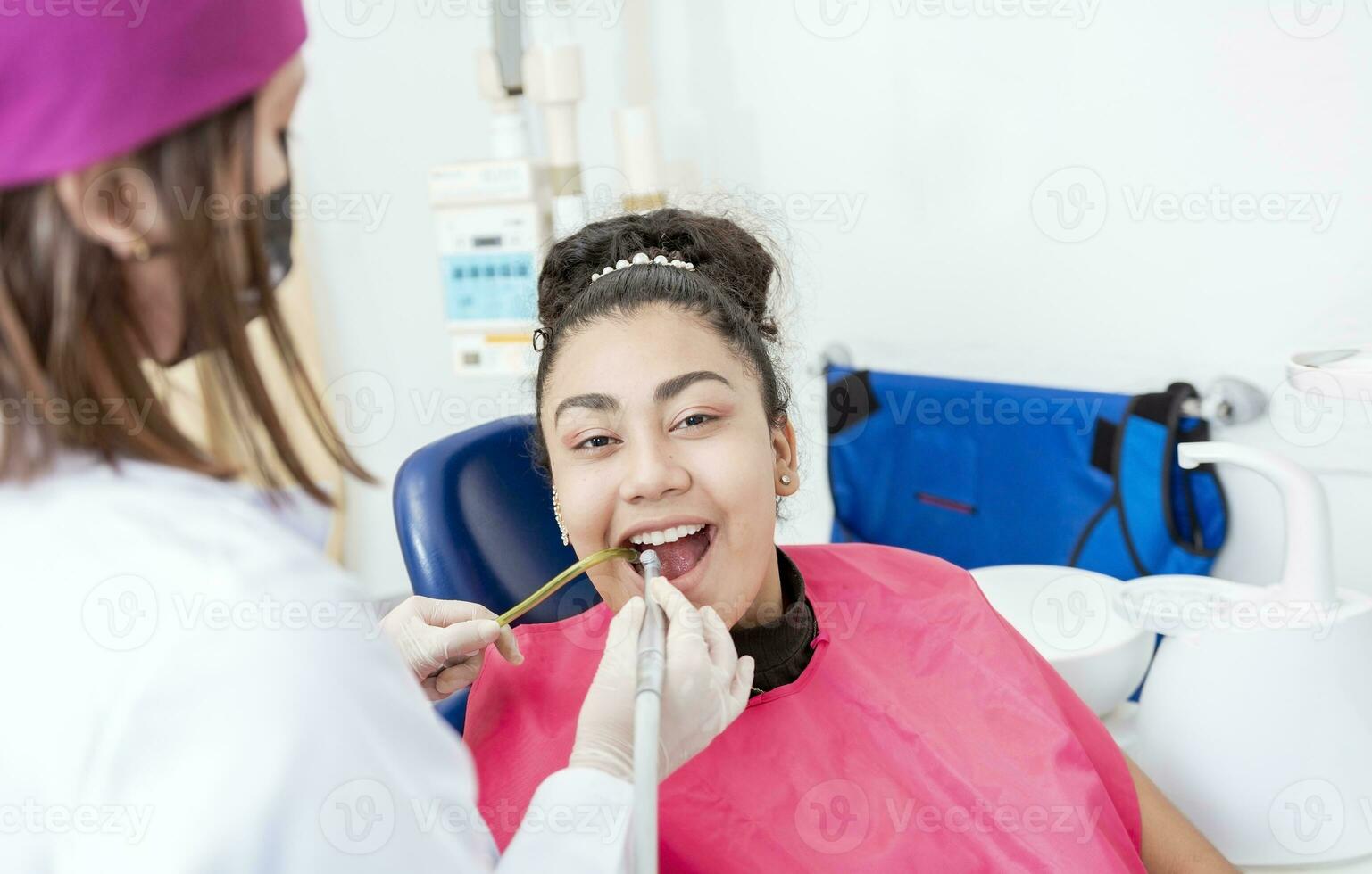 Stomatologist woman with drill cleaning patient girl mouth. Stomatologist drilling and cleaning a patient teeth, Woman stomatologist drilling patient teeth looking at the camera photo