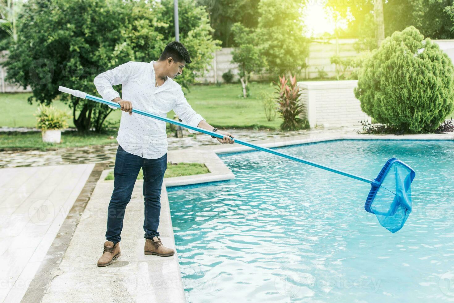 un hombre limpieza piscina con hoja desnatadora. hombre limpieza el piscina con el desnatadora, persona con desnatadora limpieza piscina, manos participación un desnatadora con azul piscina en el antecedentes foto