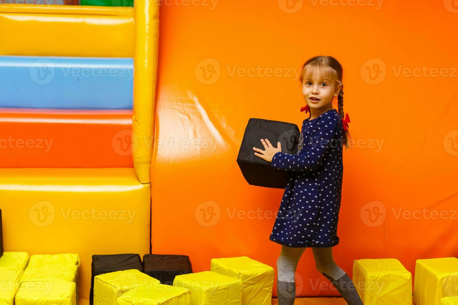 Happy laughing girl playing with toys, colorful balls in playground, ball pit, dry pool. Little cute child having fun in ball pit on birthday party in kids amusement park and play center indoor photo