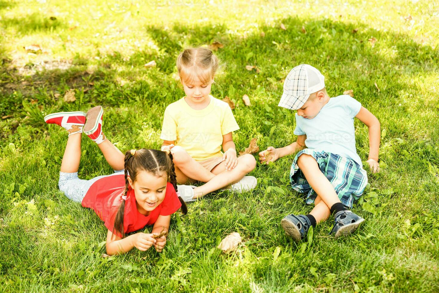 three children in the park are sitting on the grass with a phone photo