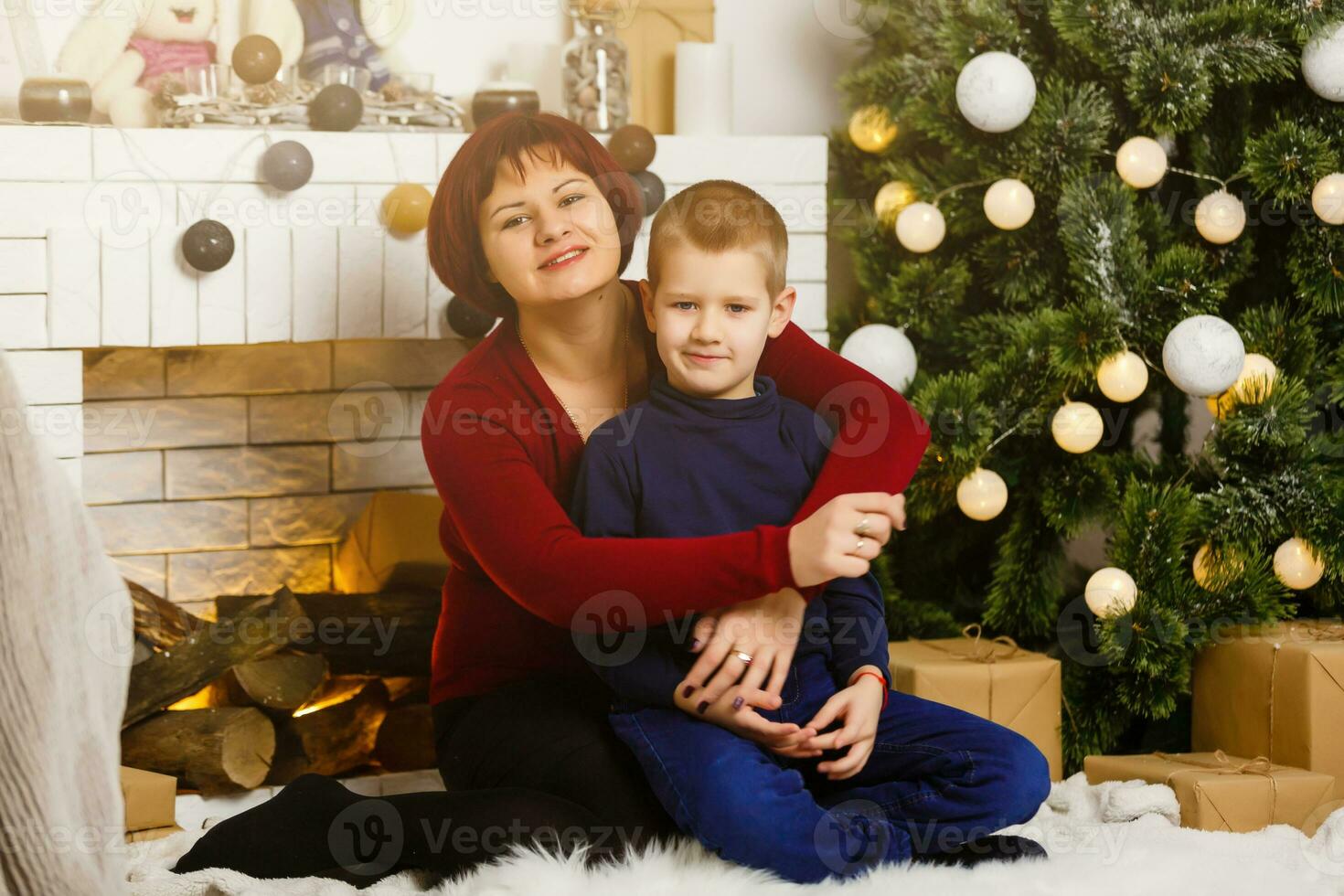 In the living room with a fireplace and a Christmas tree, mother and her son are packing a present for Christmas photo