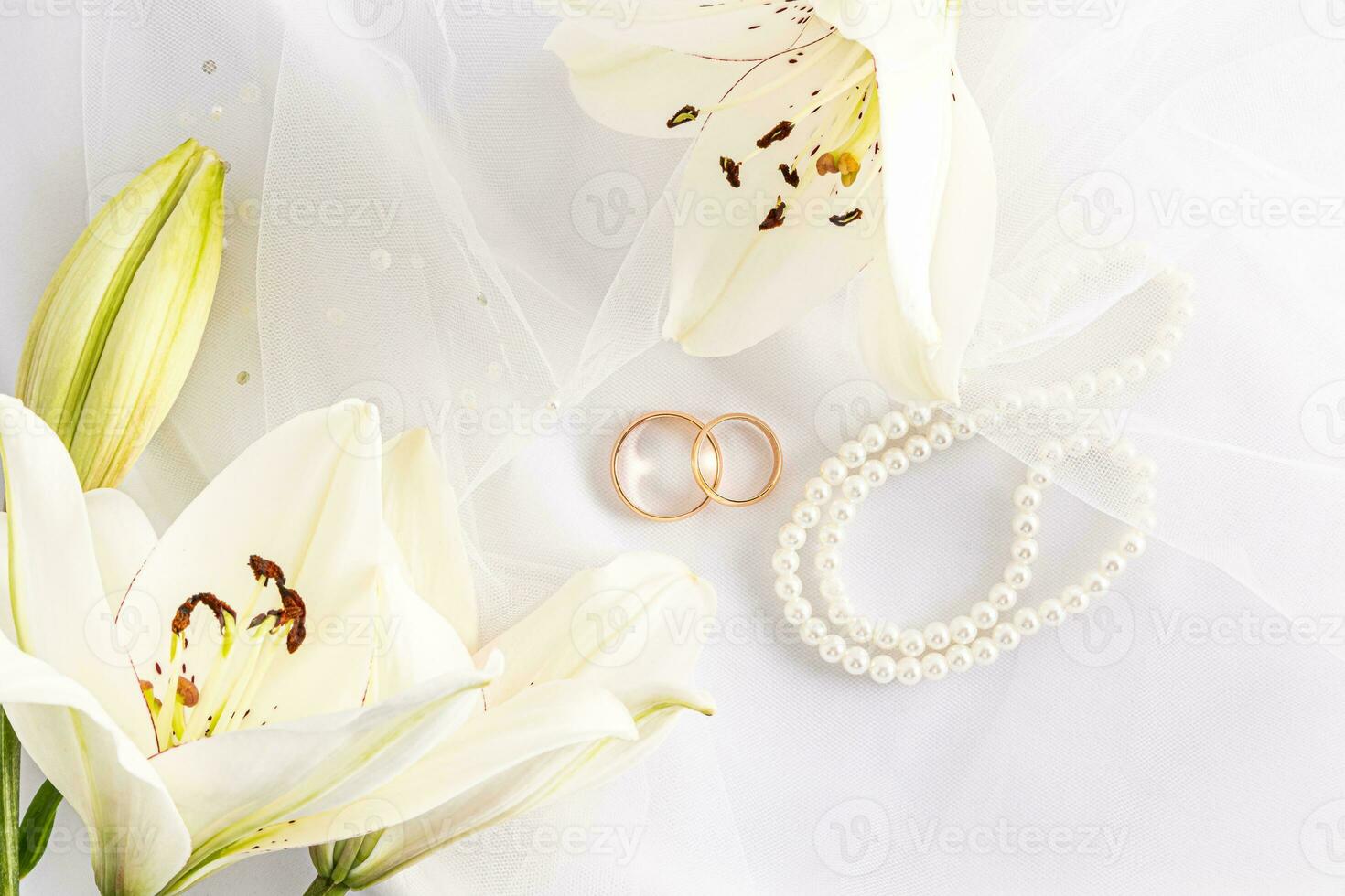 Top view of two gold wedding rings on a white bridal bridal veil and pearl beads. delicate white lilies. the concept of a wedding card, photo