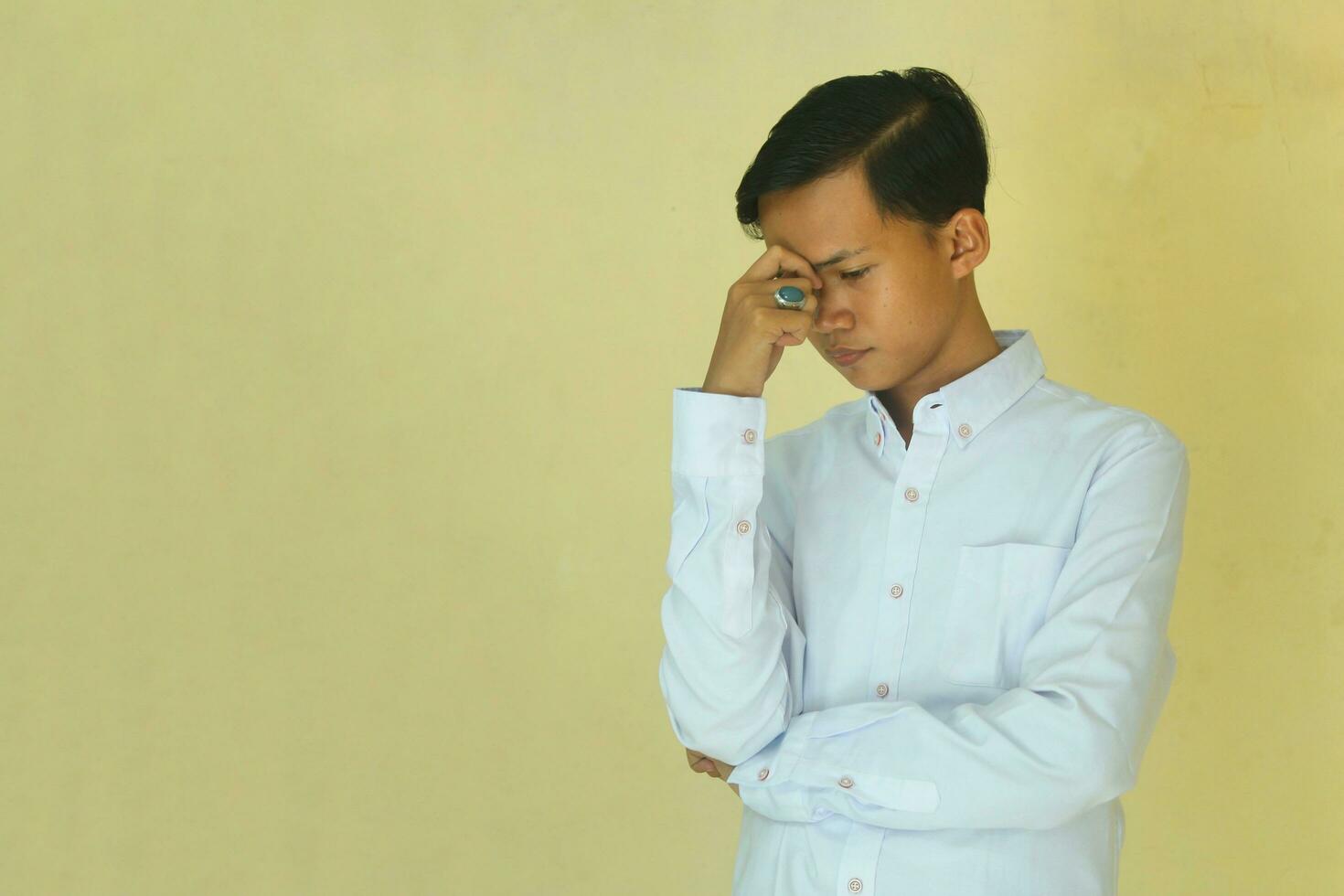 the confused, stressed, and disappointed face of the Asian youth in white.  movement of the hands over the head. photo