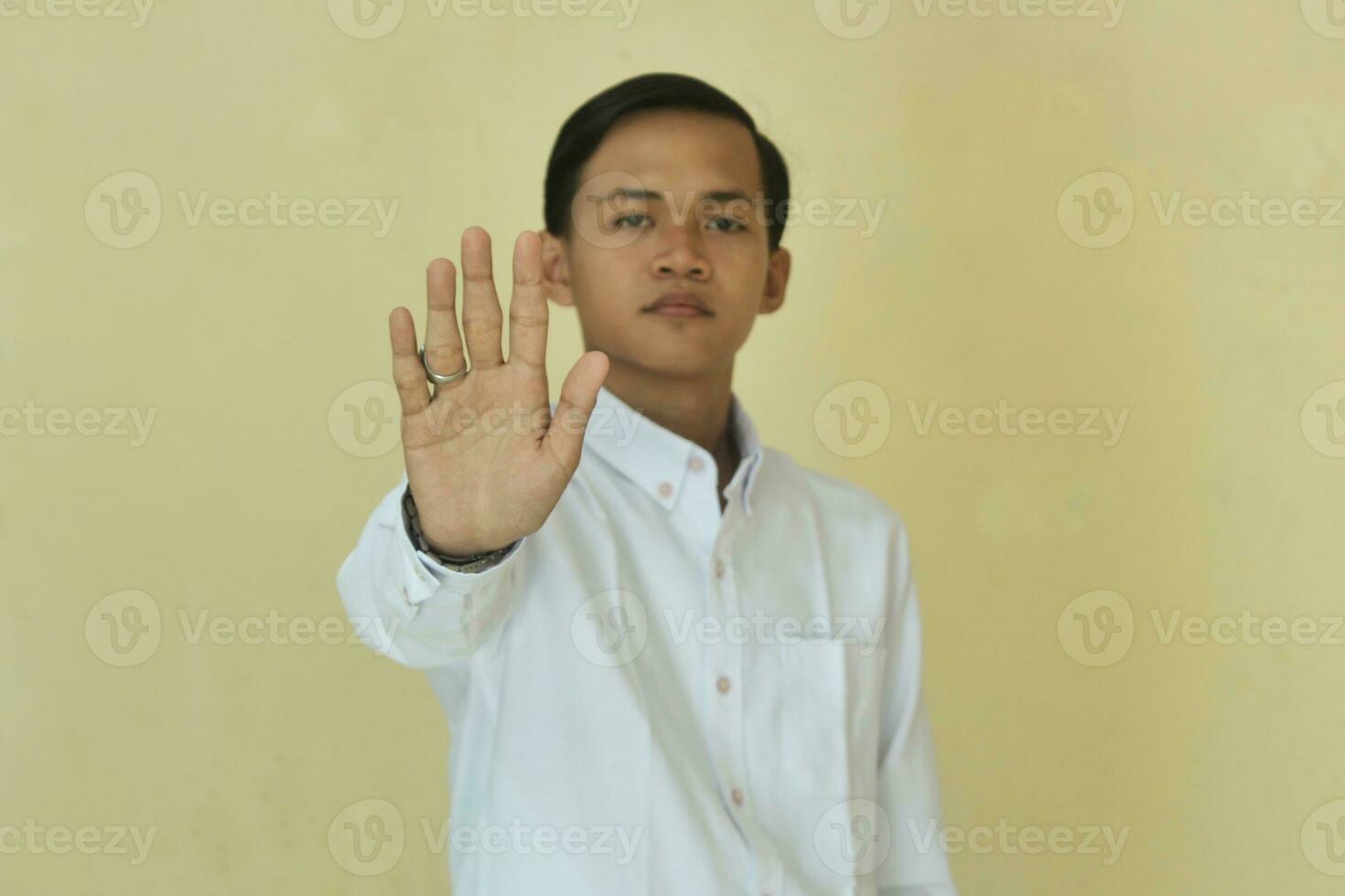 a man in a white shirt giving a stop sign or warning of danger with a palm isolated on a yellow background photo