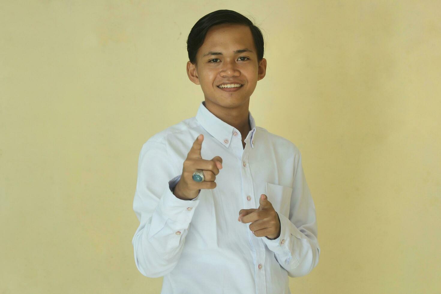 young asian man in white shirt pointing forward giving vote or agree  on yellow background photo