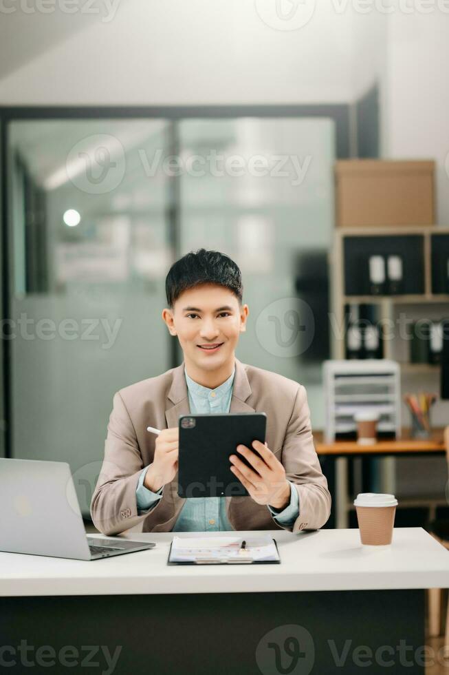 Young Asian business man working at office with laptop, tablet and taking notes on the paper. photo