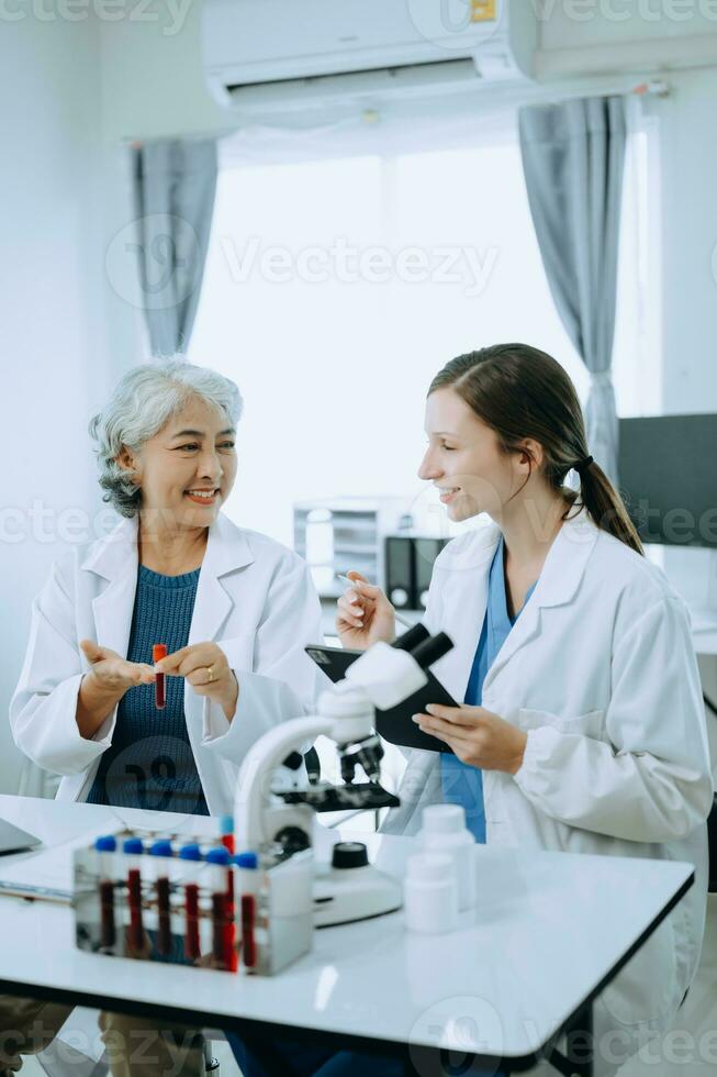 Two scientist or medical technician working, having a medical discuss meeting with an Asian senior female scientist supervisor in the laboratory with online reading, test samples and innovation photo