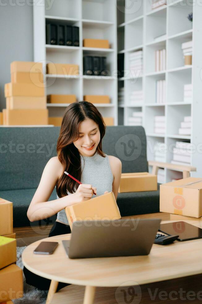 Startup small business SME, Entrepreneur owner woman using smartphone or tablet taking receive and checking online purchase shopping order to preparing pack product box. photo