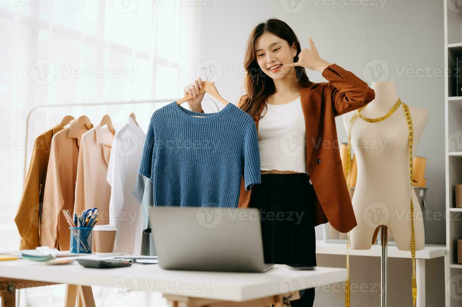 asiático joven mujer en escritorio en oficina de Moda diseñador y sostiene tableta, ordenador portátil y teléfono inteligente en blanco mesa foto