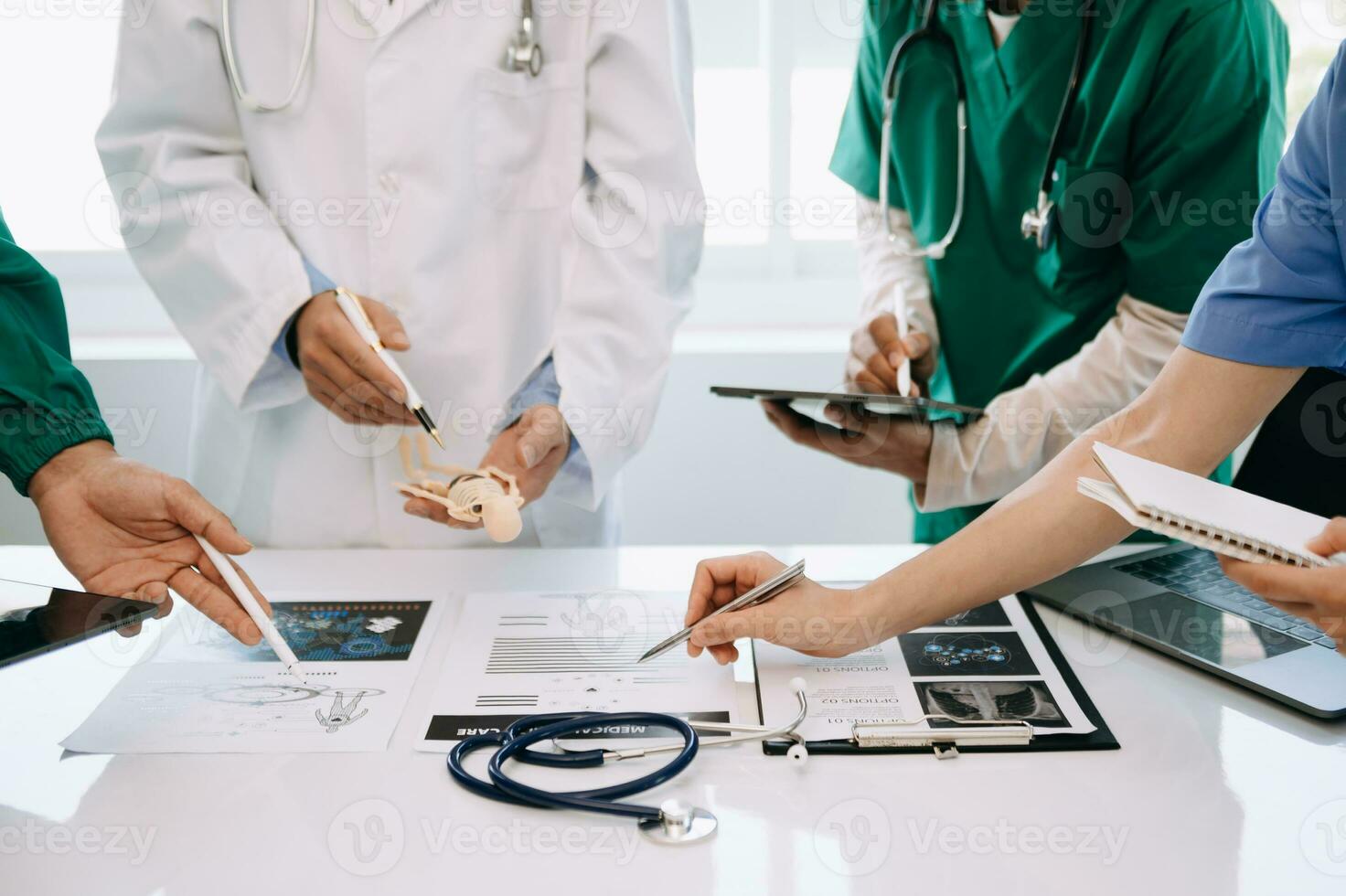 Medical team having a meeting with doctors in white lab coats and surgical scrubs seated at a desk discussing a patients working online using computers in the medical industry photo