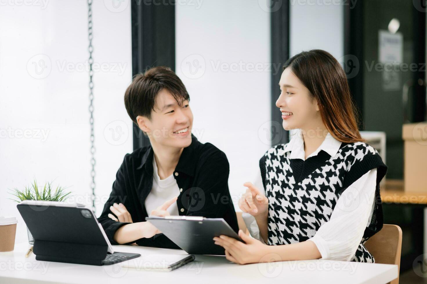 Asian business colleague business presents and explains and using laptop and tablet. Teamwork, financial marketing team, while sitting in modern office room. photo