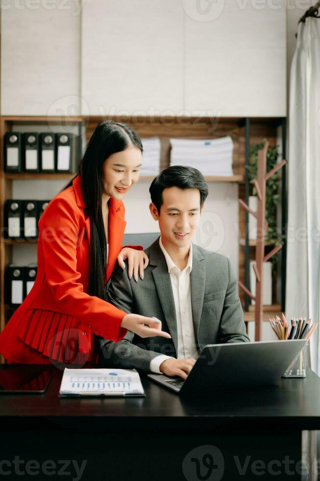 Asian business colleague business presents and explains and using laptop and tablet. Teamwork, financial marketing team,   while sitting in office room. photo