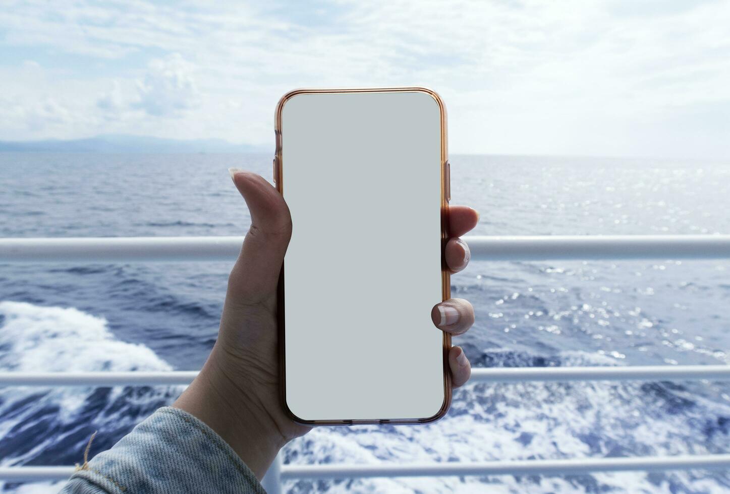 Mockup image of a woman hand holding white mobile phone with blank white screen on the ferryboat in front of the turquoise sea and sky. photo