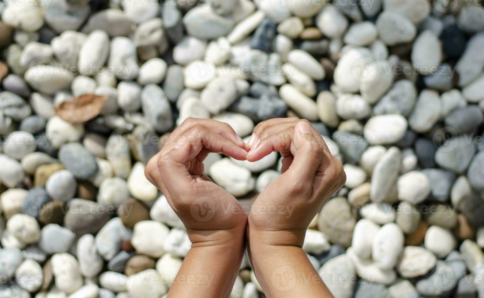 Female hand making heart symbol, blurred stones as background. Love concept on Valentine day. photo