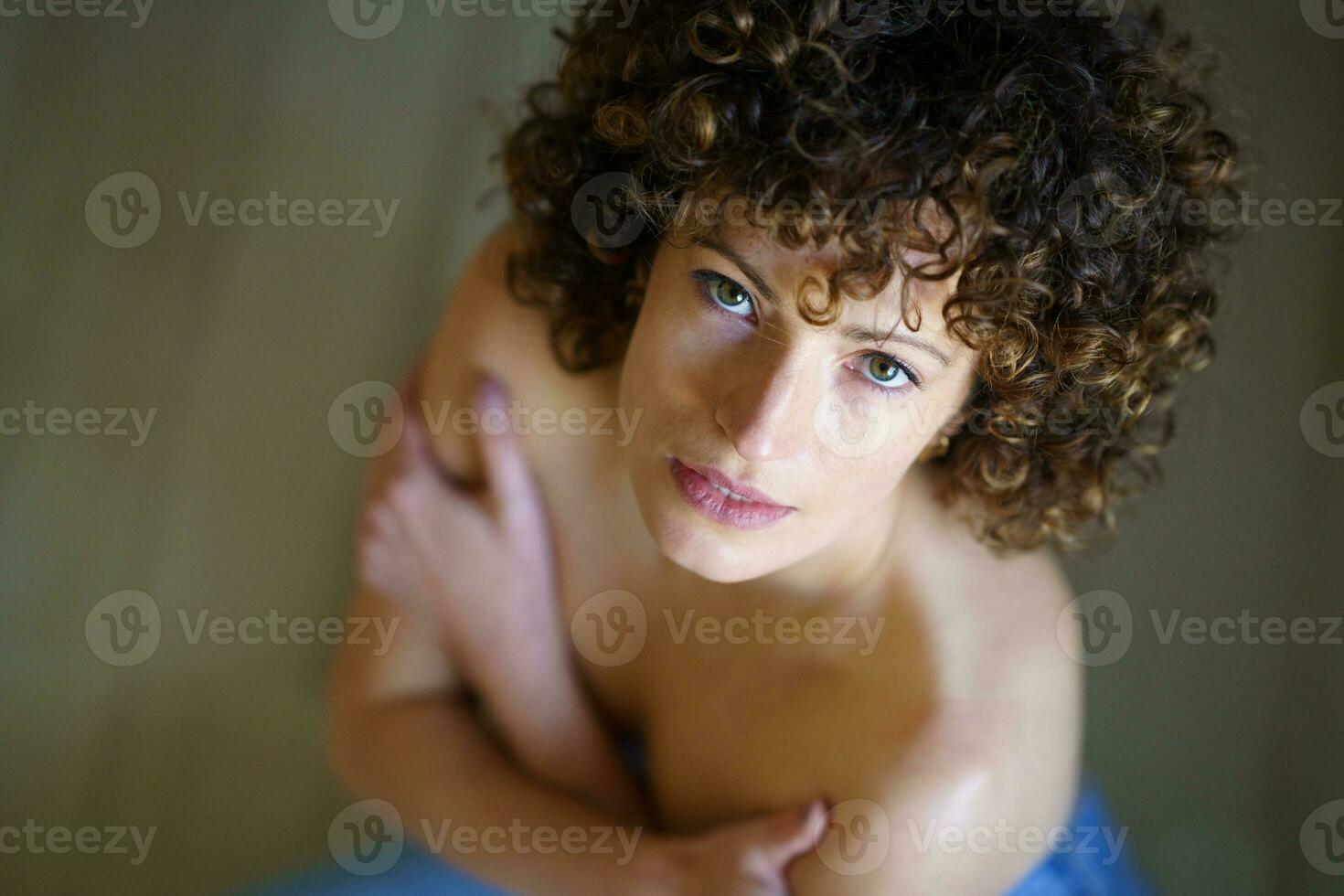 High angle of curly-haired woman with her bare shoulders looking at camera photo